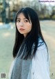 A woman with long black hair wearing a white shirt and a gray scarf.