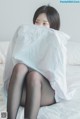 A woman sitting on a bed covered in a white sheet.