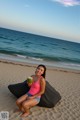 A woman sitting on a bean bag on the beach holding a coconut.