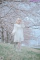 A woman in a white dress standing in front of a tree.