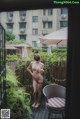 A naked woman standing on a balcony next to a chair.