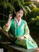 A woman in a green and yellow hanbok sitting on a bench.